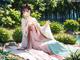 A woman in a kimono sitting on a blanket in a park.