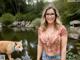 A woman wearing glasses standing next to a fox in a pond.