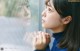 A young woman looking out of a window with her hands clasped together.