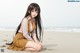 A girl sitting on the beach with long black hair.