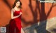 a woman in a red dress leaning against a wall