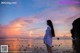 A woman standing on a beach looking at the sunset.