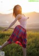 A woman in a pink tank top and plaid skirt dancing in a field.