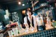 A woman behind a bar with bottles of alcohol on the counter.